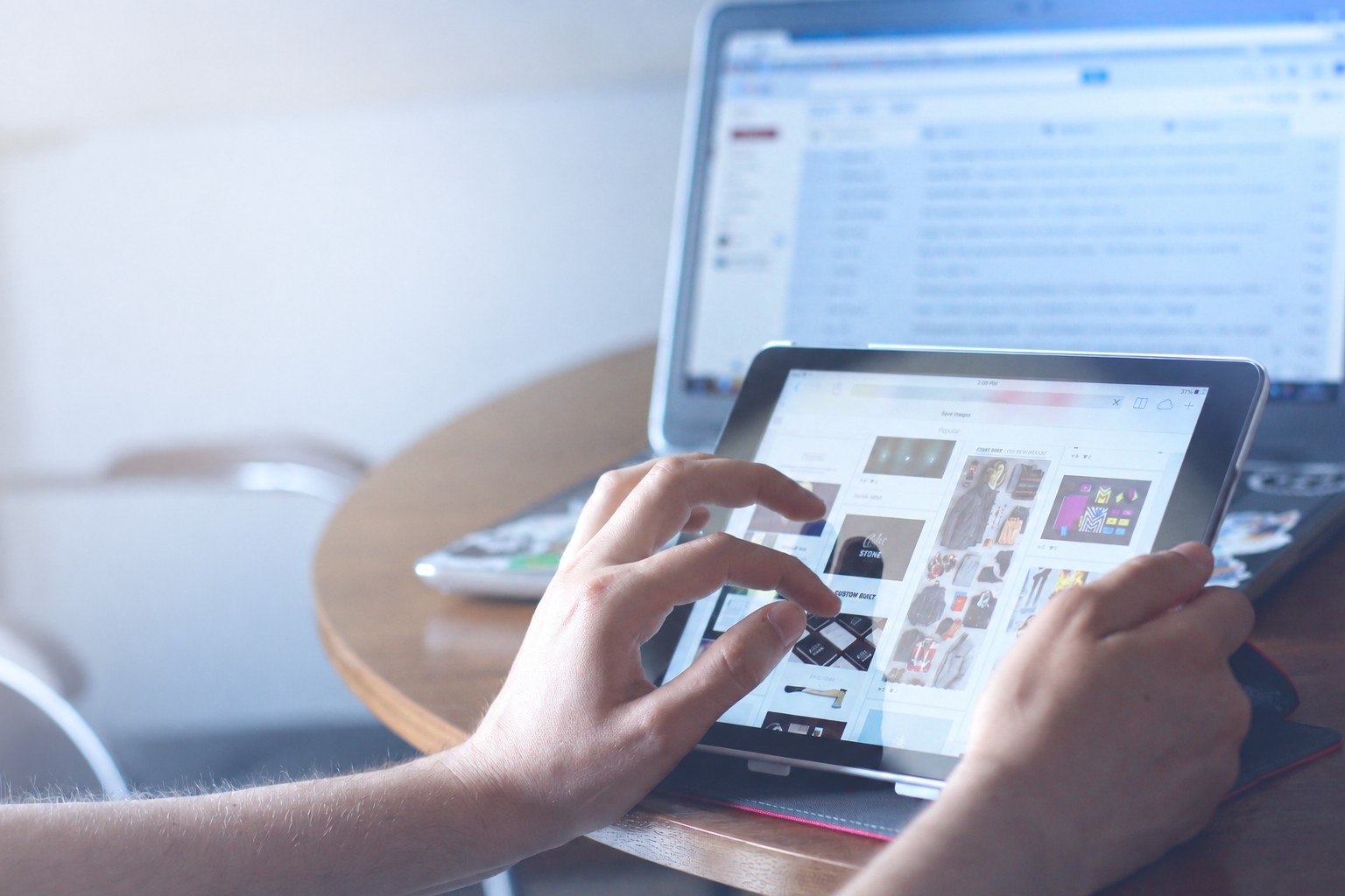 Close-up of hands using a tablet, with a laptop open in the background